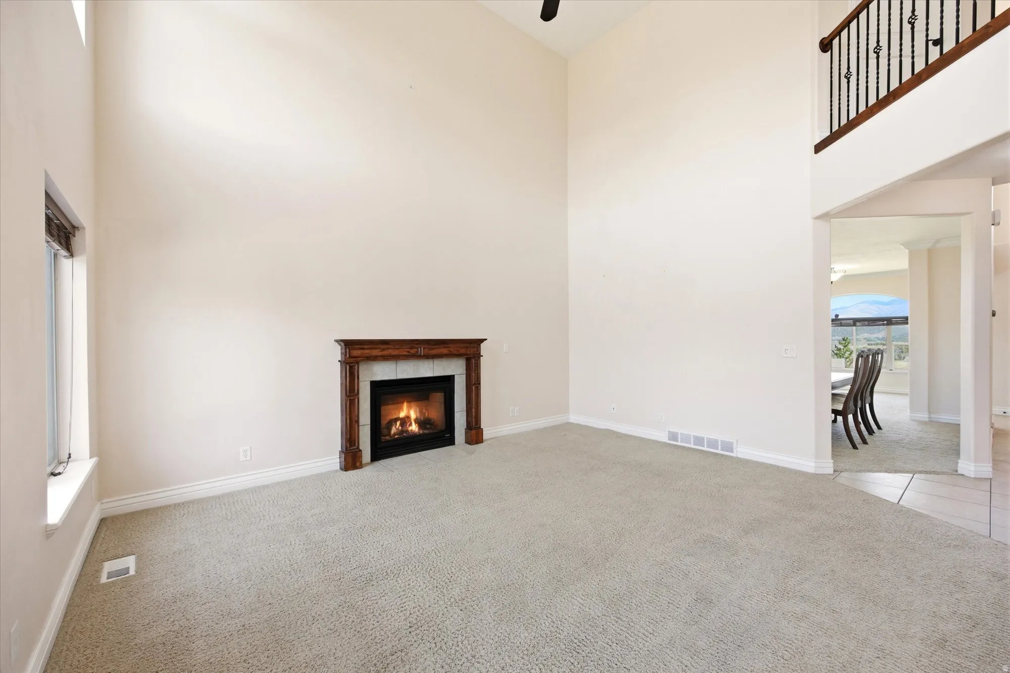 Great room featuring a fireplace with a wood mantle and tile surround, high ceilings, and light-toned carpet flooring