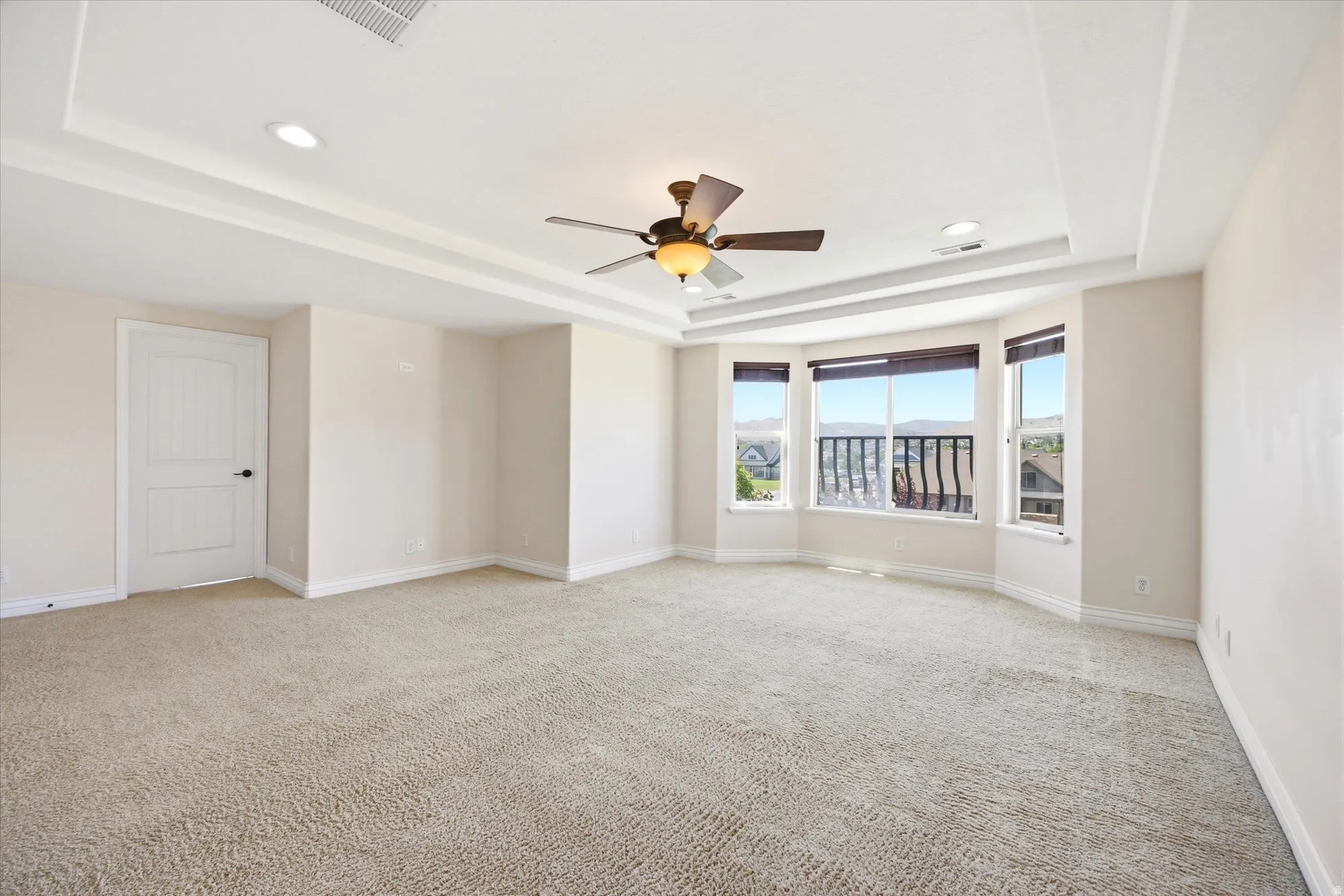 Spacious room featuring neutral carpeting, a tray ceiling with recessed lighting, and a ceiling fan