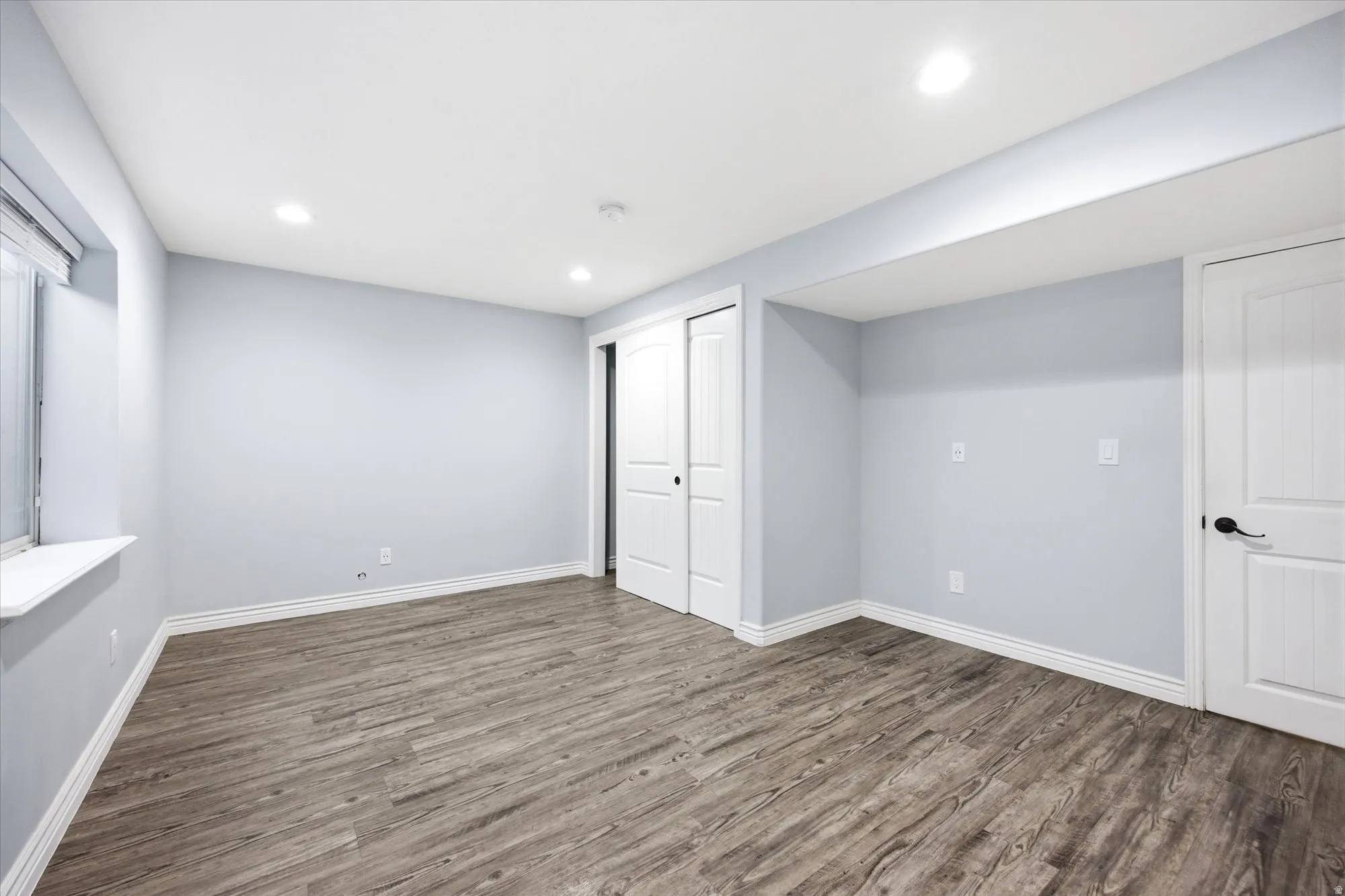 Spacious room featuring wood-finish flooring, recessed lighting, and a window with a white sill