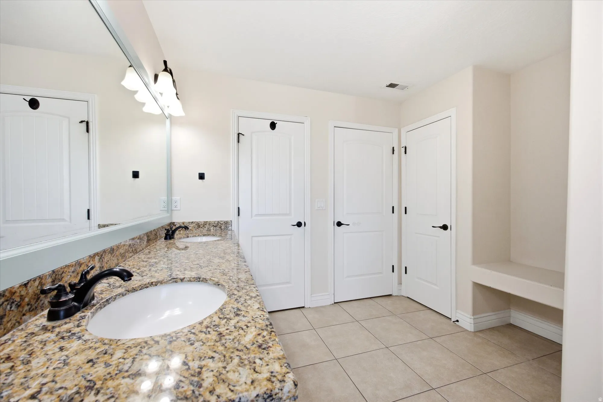 Bathroom featuring a dual vanity with undermount sinks, granite countertops, and dark bronze fixtures