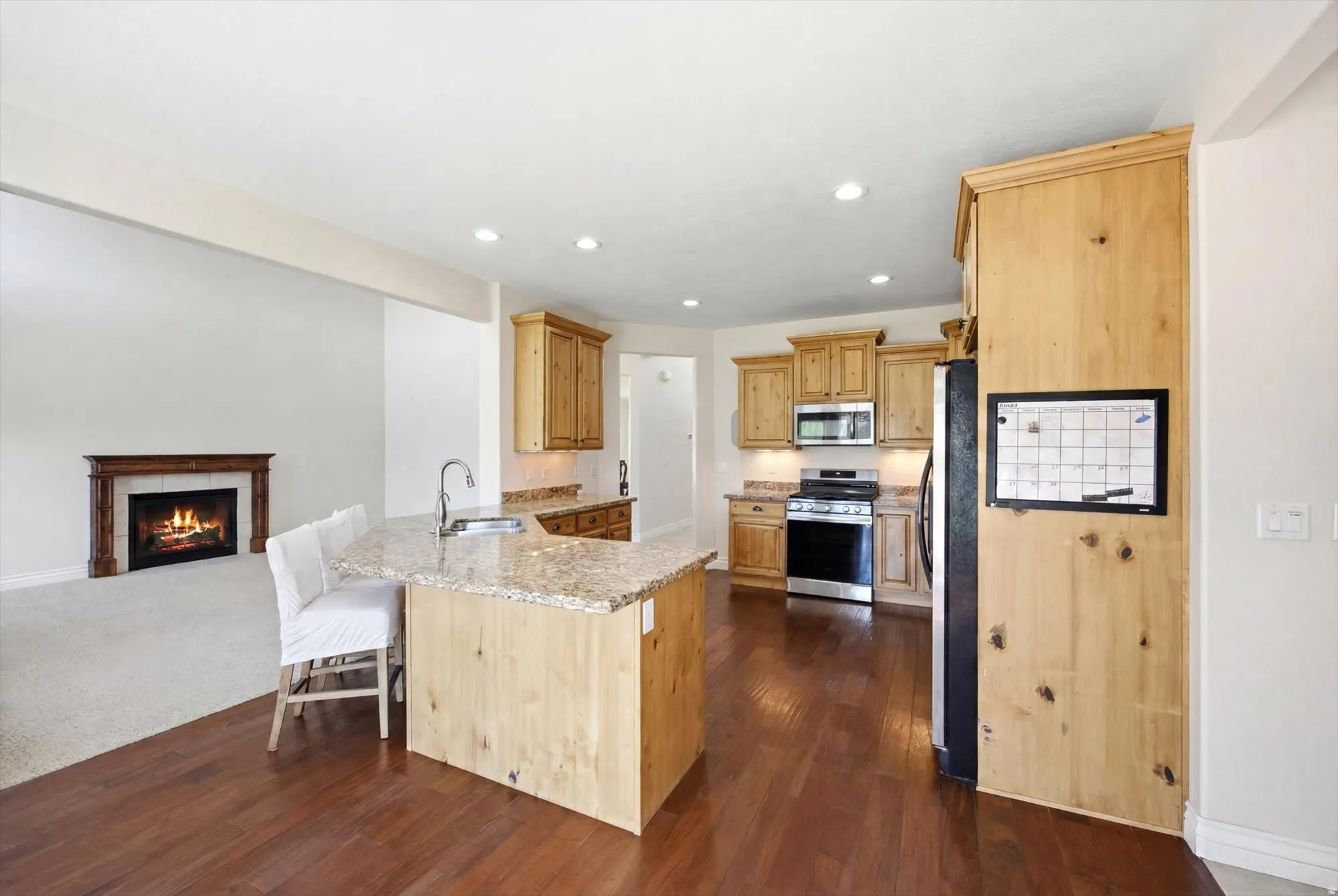 Kitchen featuring light wood cabinetry, stone countertops, and a stainless steel appliance suite including a microwave, range, and refrigerator