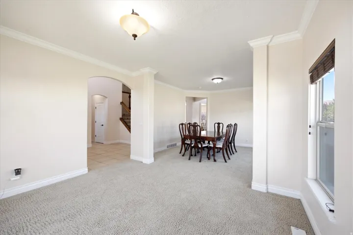 Spacious open concept living area featuring neutral carpeting, crown molding, an arched entryway, recessed lighting, and a bay window