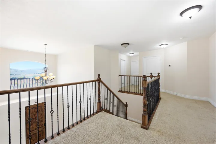 Upper-level landing featuring textured carpeting, wood-finish and wrought iron railings, an arched window, and recessed ceiling lighting