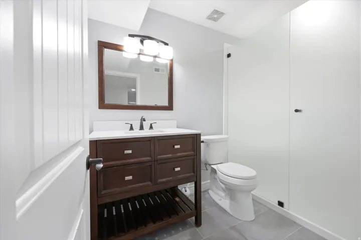 Bathroom featuring a wood-finish vanity with a white countertop and rectangular sink, complemented by a framed mirror and a three-light fixture