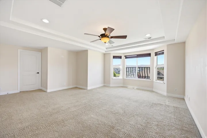 Spacious room featuring neutral carpeting, a tray ceiling with recessed lighting, and a ceiling fan