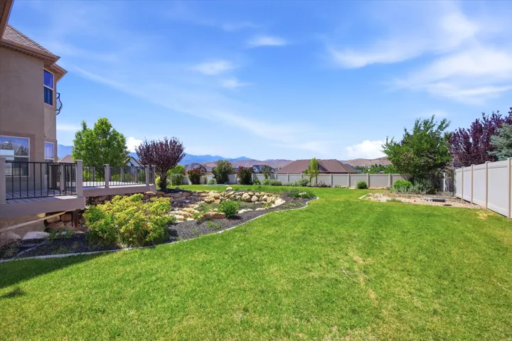 Expansive backyard featuring a manicured lawn, a multi-level deck with dark railing, and a decorative rock garden with varied plantings