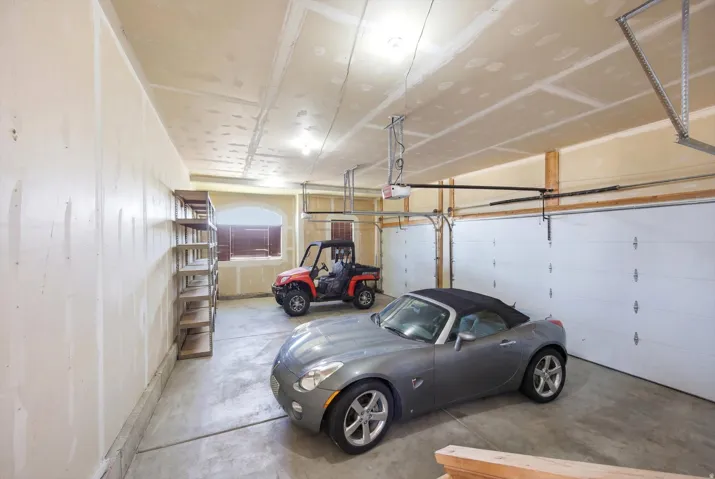 Spacious garage featuring two overhead doors, exposed wood framing, concrete flooring, and an arched window