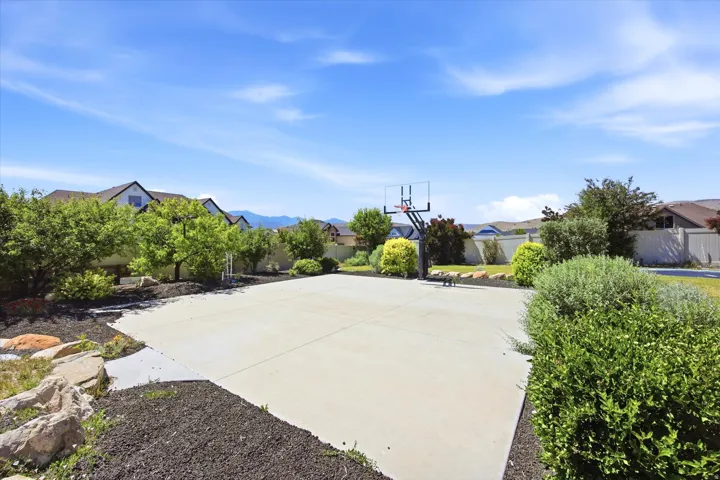 Concrete sport court with a basketball hoop, surrounded by mature landscaping and decorative rock features