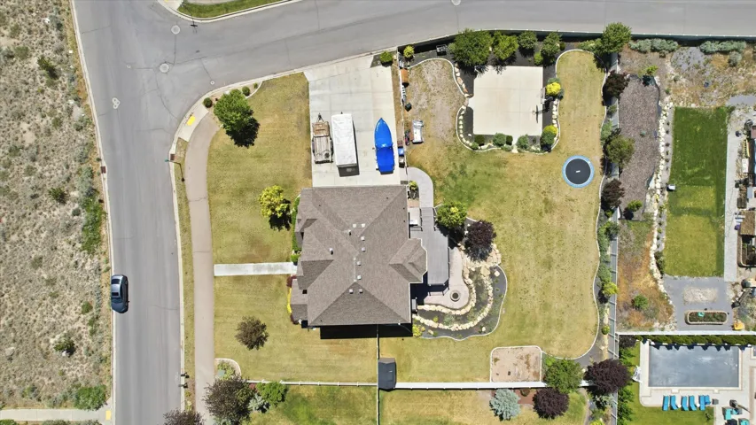 Expansive property featuring a large house with a multi-gabled roof, extensive green lawn areas, a decorative rock water feature, and a paved sport court
