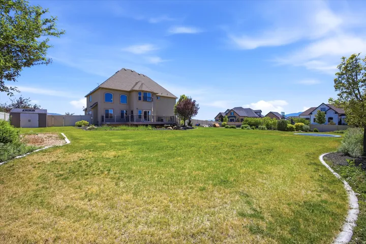 Expansive backyard featuring a large green lawn, a multi-level deck, and a detached storage shed