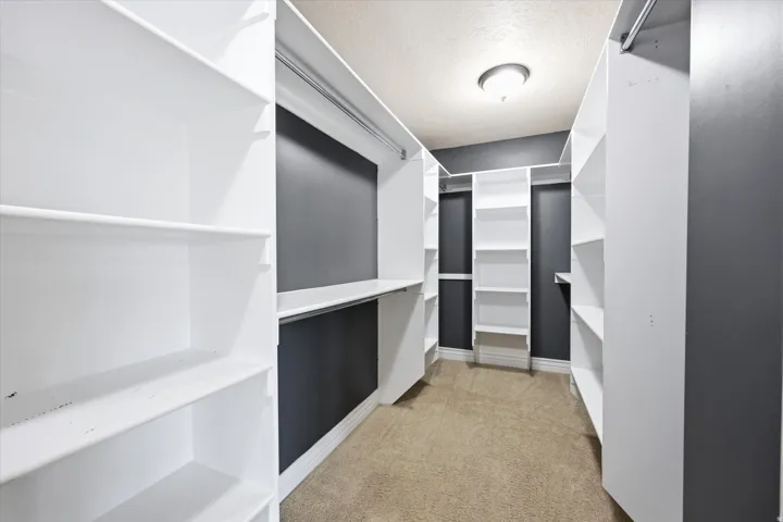 Walk-in closet featuring extensive white shelving, multiple hanging rods, and a neutral carpeted floor
