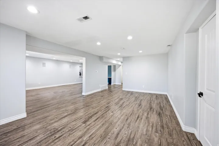 Expansive open-concept living area featuring wood-finish flooring, recessed lighting, neutral wall paint, white baseboards, and a white paneled door with matte black hardware