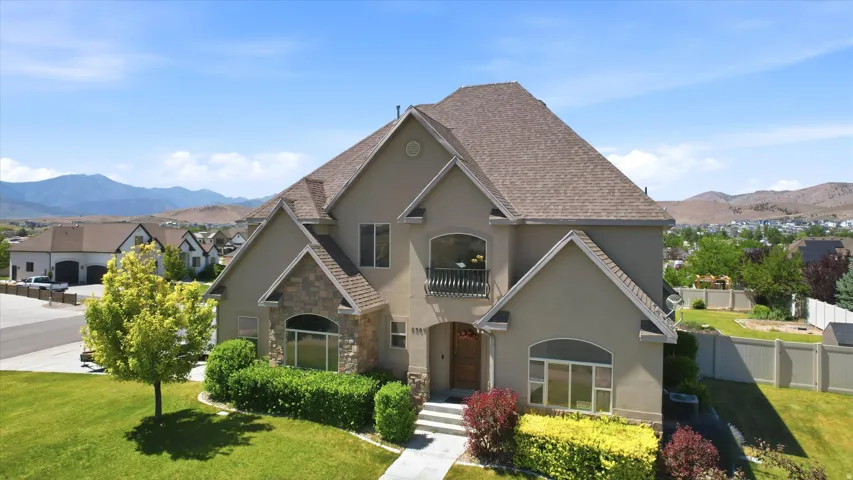 Stucco residence featuring a stone facade accent, multi-level roofline, and established landscaping