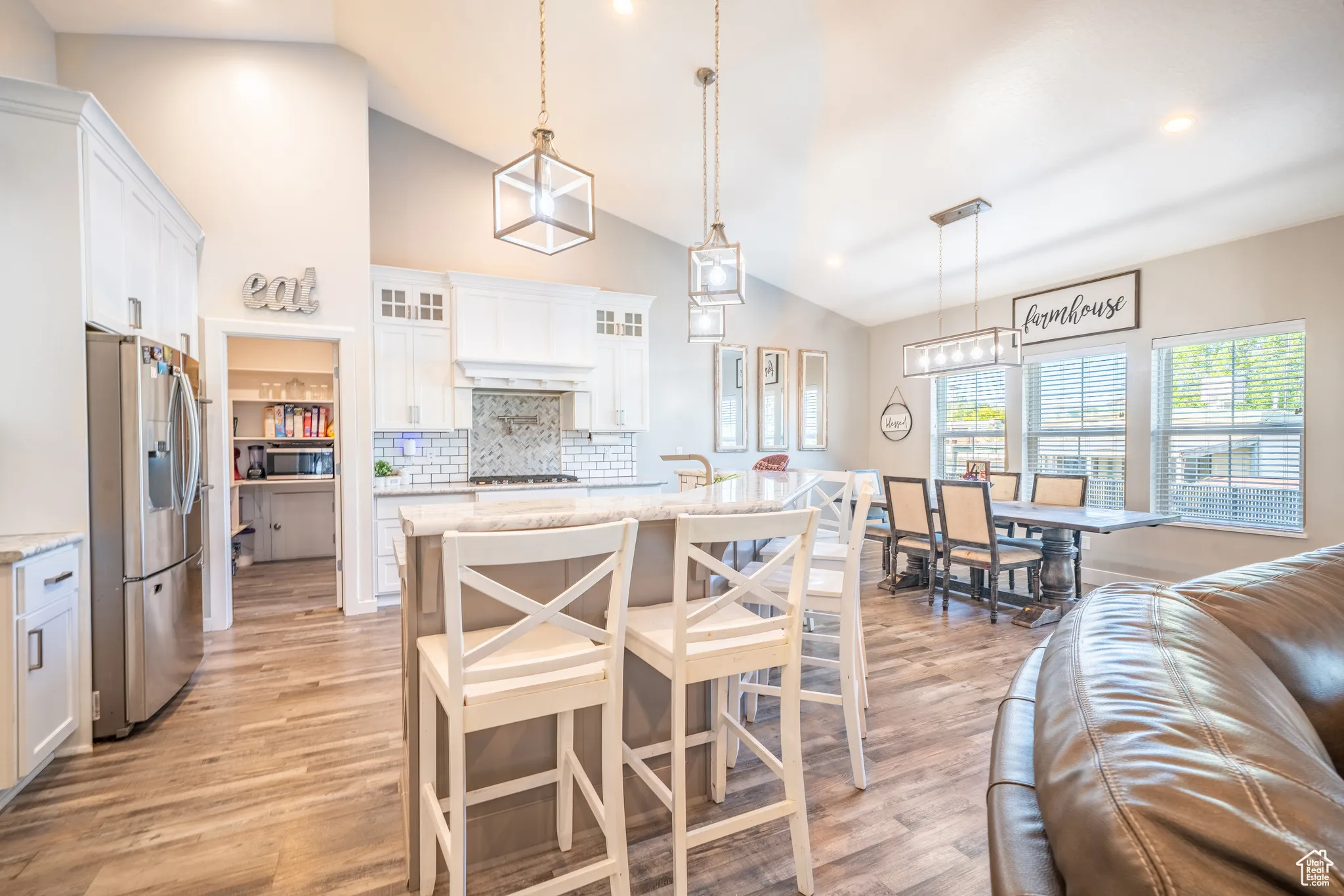 Open-concept kitchen and dining area featuring vaulted ceilings, wood-finish flooring, white cabinetry, a kitchen island with seating, and a pantry with built-in shelving