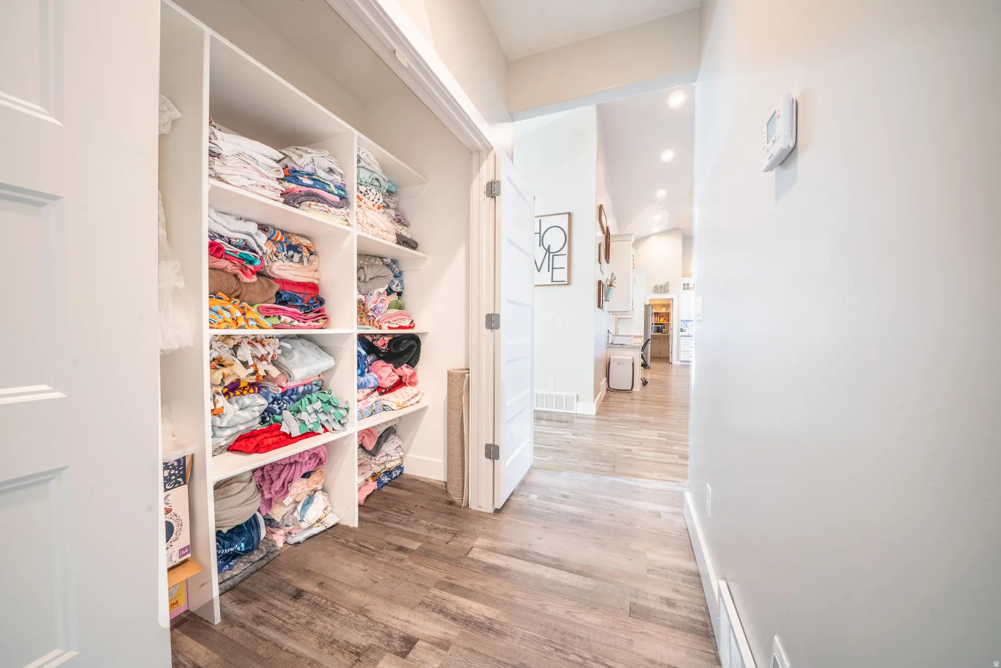 Integrated hallway storage featuring white shelving units, wood-finish flooring, and recessed lighting