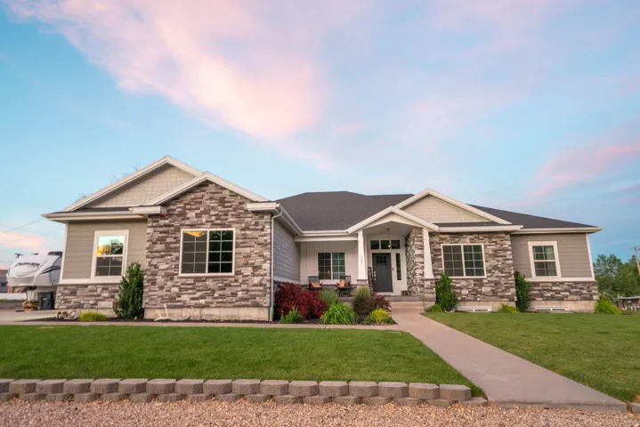Contemporary ranch-style home featuring a prominent stone facade, gray siding, and gabled rooflines