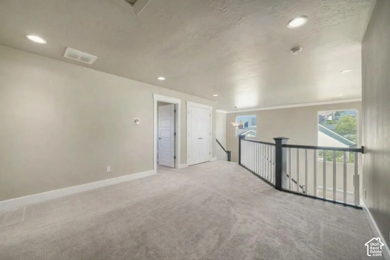 Carpeted open area featuring white trim, a painted railing, recessed lighting, and two windows