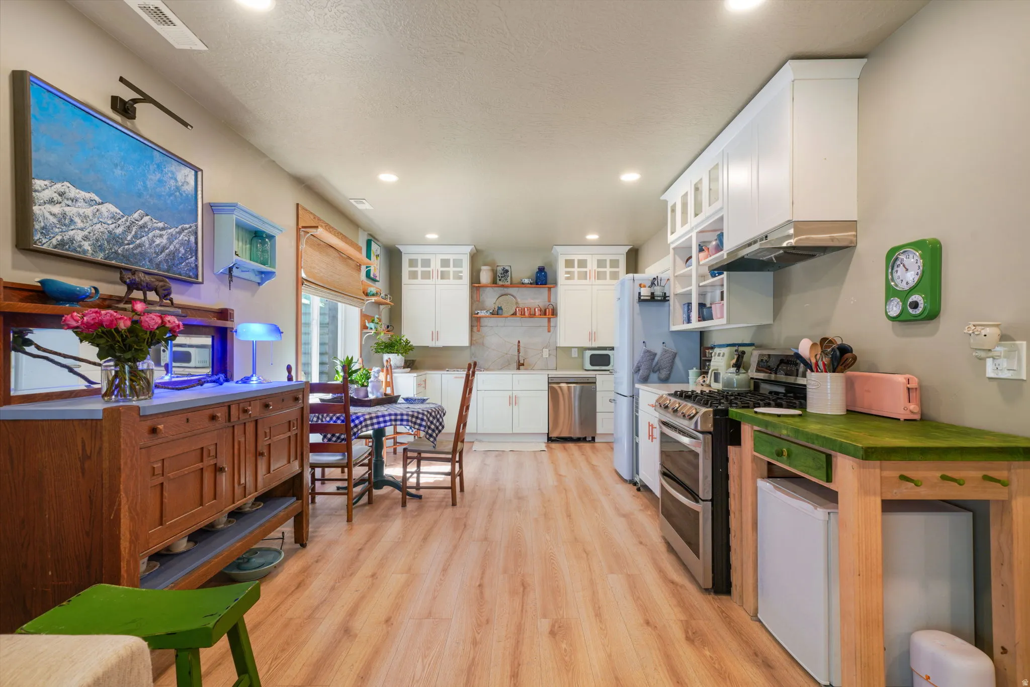 Open-concept kitchen and dining area featuring light wood-finish flooring, white cabinetry, stainless steel appliances, a window with horizontal blinds, and recessed lighting