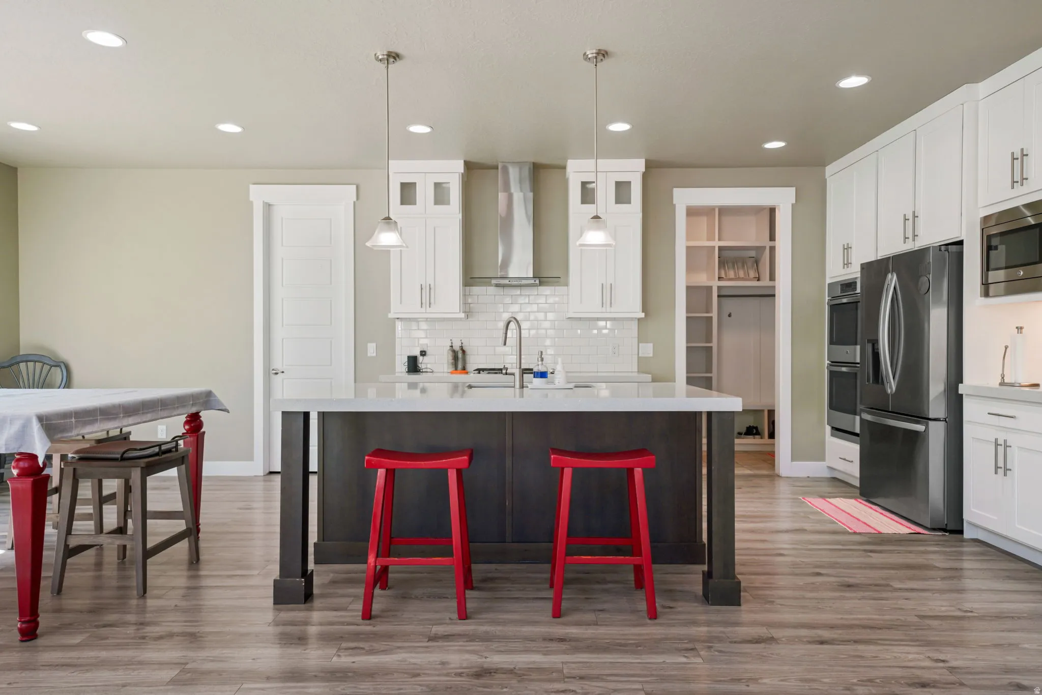 Open-concept kitchen featuring an island with a light-toned countertop, wood-finish flooring, white cabinetry with contemporary hardware, stainless steel appliances, and recessed lighting