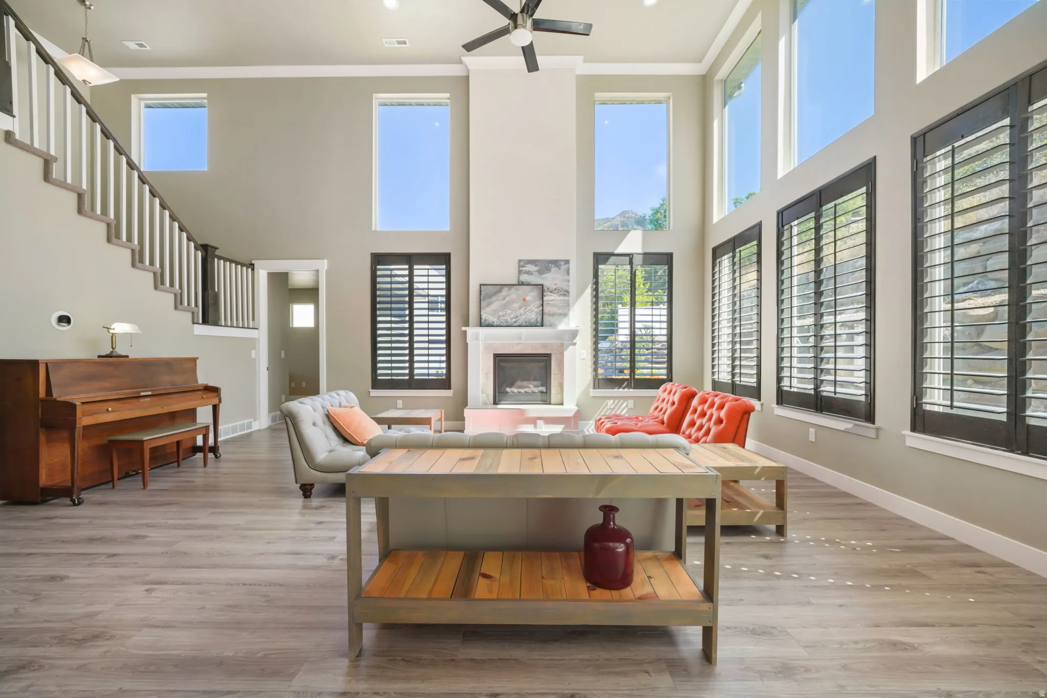 Great room featuring high ceilings, wood-finish flooring, a fireplace with a stone surround, and multiple tall windows with plantation shutters