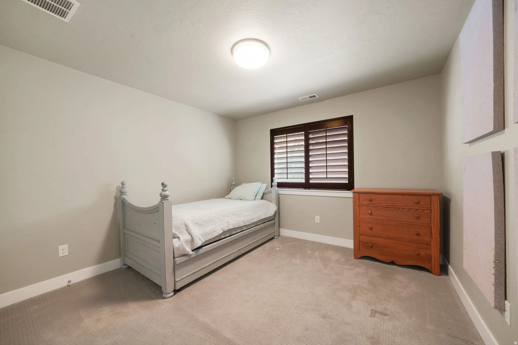 Carpeted interior room featuring light gray walls, white baseboards, and a window with dark wood shutters