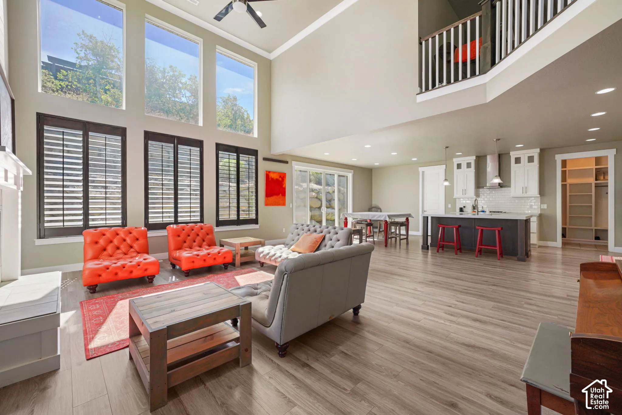 Two-story living area with high ceilings, wood-finish flooring, a white mantel, and a multi-level window arrangement featuring lower plantation shutters