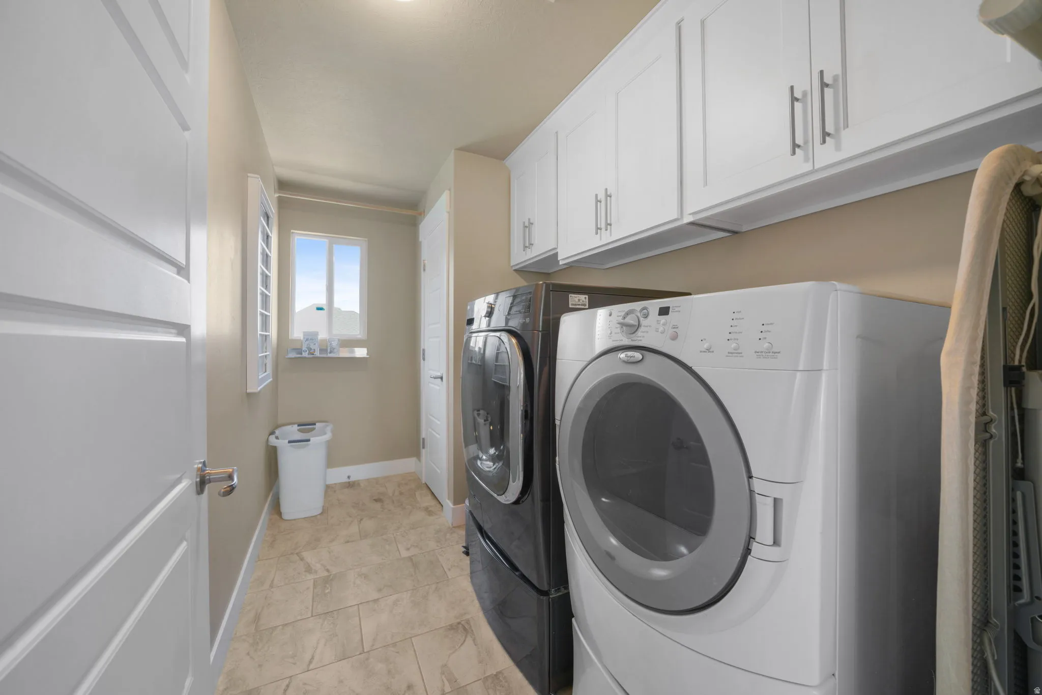 Dedicated utility space featuring ample white cabinetry, tile flooring, and a window with natural light