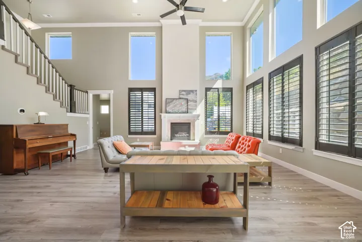 Great room featuring high ceilings, wood-finish flooring, a fireplace with a stone surround, and multiple tall windows with plantation shutters