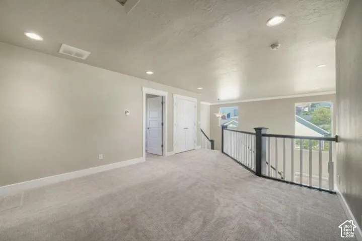 Carpeted open area featuring white trim, a painted railing, recessed lighting, and two windows