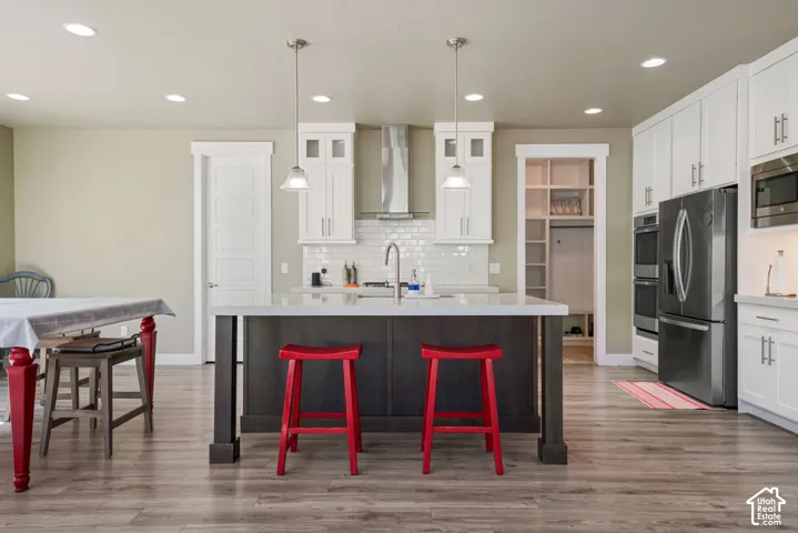 Open-concept kitchen featuring an island with a light-toned countertop, wood-finish flooring, white cabinetry with contemporary hardware, stainless steel appliances, and recessed lighting
