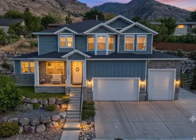 Two-story exterior with blue siding and stone accents, two-car garage, covered porch, and well-lit entry stairs