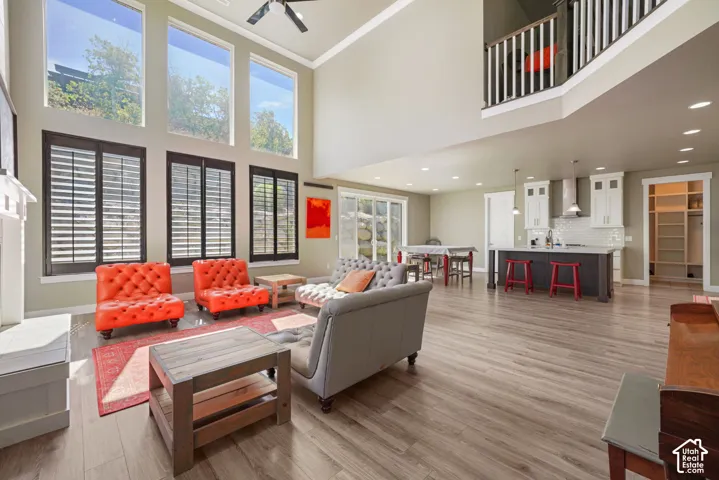 Two-story living area with high ceilings, wood-finish flooring, a white mantel, and a multi-level window arrangement featuring lower plantation shutters