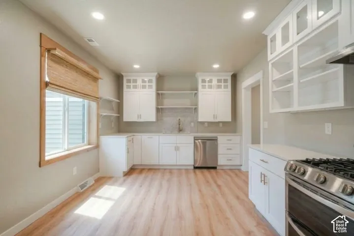White cabinetry, stainless steel appliances, wood-finish flooring, white countertops, and recessed lighting