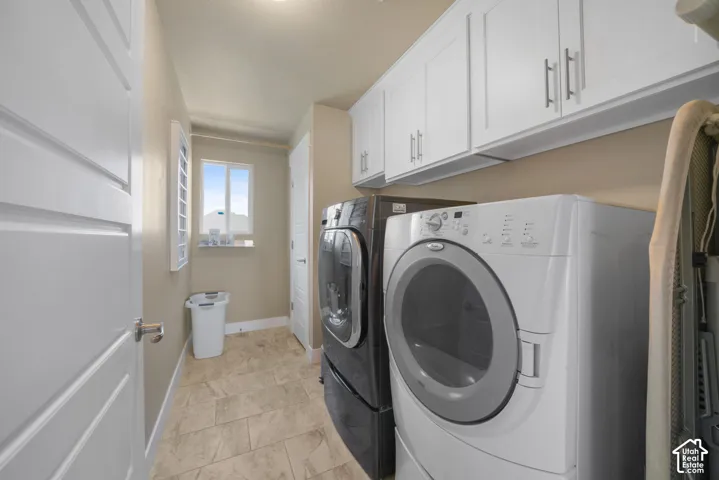 Dedicated utility space featuring ample white cabinetry, tile flooring, and a window with natural light