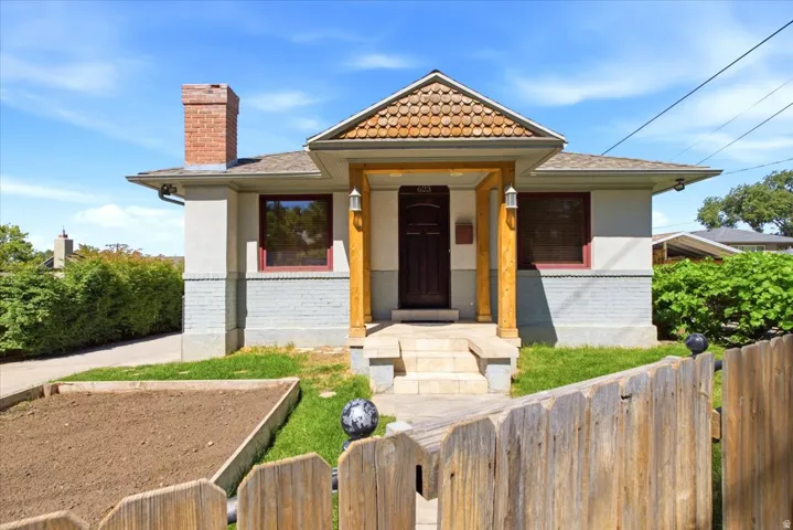 Stucco exterior with a brick chimney, covered front porch, and wood-shingle detail