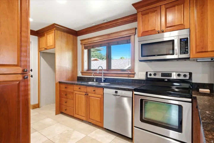 Kitchen featuring wood-finish cabinetry, stainless steel appliances, dark stone countertops, and a tile floor