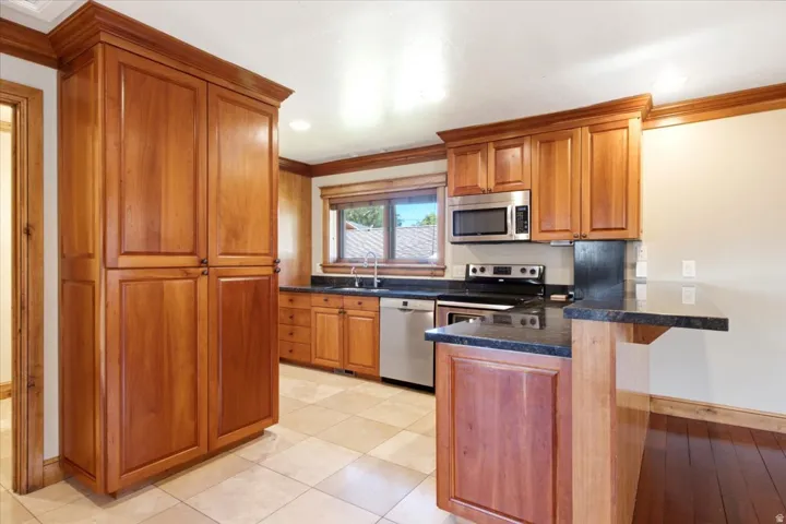Kitchen featuring extensive wood cabinetry, dark countertops, tile flooring, stainless steel appliances, and a breakfast bar