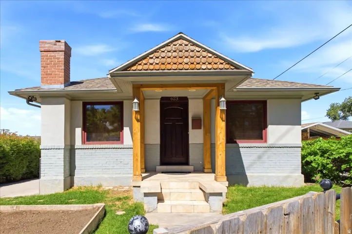 Craftsman-style home featuring a brick chimney, a covered entry with wood posts, and a decorative shingle facade