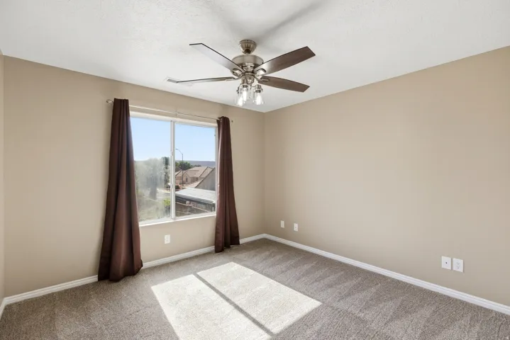 Carpeted room with a ceiling fan light fixture, light-toned walls, and a window with a brown curtain rod