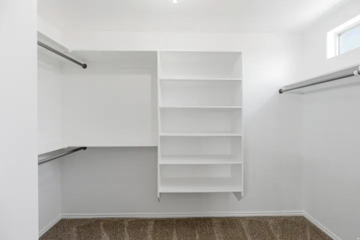 Walk-in closet featuring white built-in shelving, multiple hanging rods, and a high window for natural light