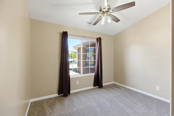 Carpeted room featuring a ceiling fan with light fixture, vaulted ceiling, and a large window with white trim
