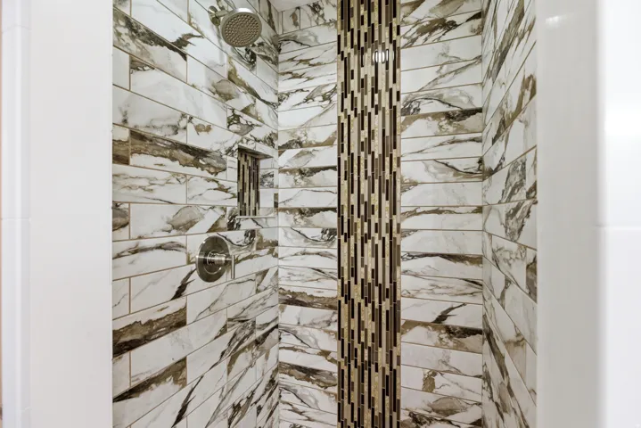 Shower with marbled tile walls, mosaic accent strip, built-in niche, and brushed nickel fixtures
