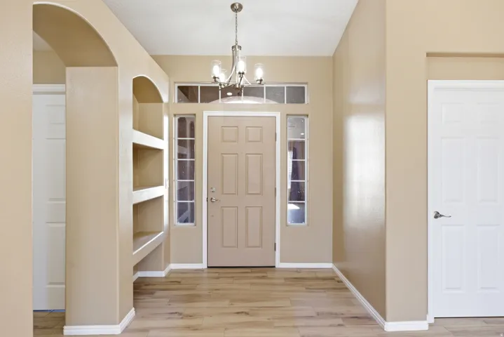 Inviting entryway featuring a paneled front door with sidelight windows and transom, built-in arched shelving, wood-finish flooring, and a brushed nickel chandelier