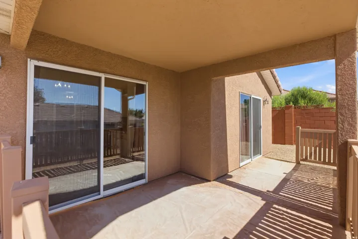 Covered patio with textured stucco walls, dual sliding glass doors, and a wood railing