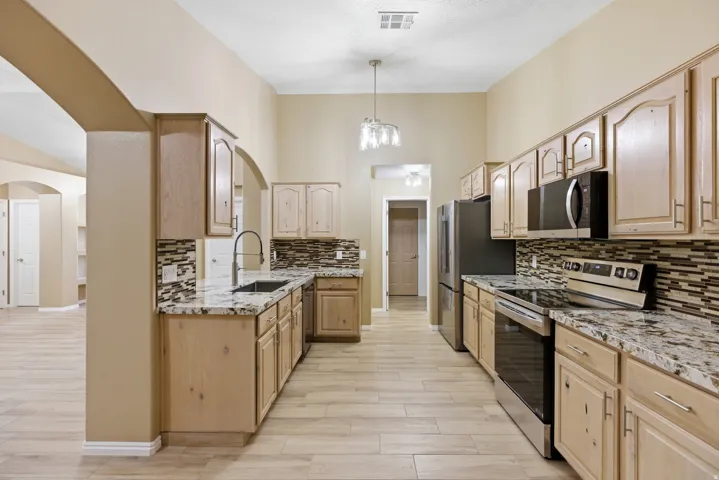 Galley kitchen featuring light wood cabinetry, stone countertops, and a mosaic tile backsplash