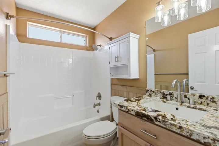 Bathroom featuring a built-in tub with a white tile surround, a transom window, and a vanity with a stone countertop and an undermount sink