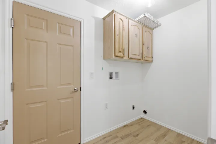 Laundry area featuring light wood-finish flooring, white walls, and built-in wood cabinetry