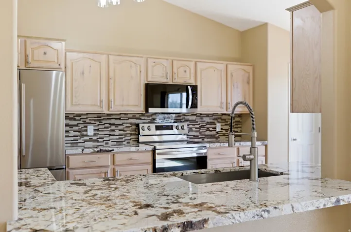 Kitchen featuring light wood cabinetry, granite countertops, stainless steel appliances, and a mosaic tile backsplash
