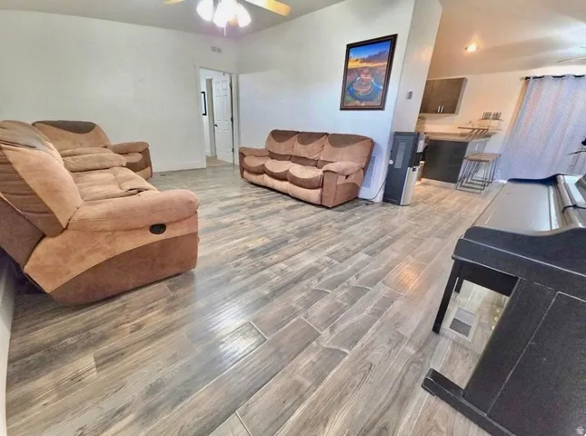 Spacious living area featuring wood-finish flooring, a ceiling fan, and white walls
