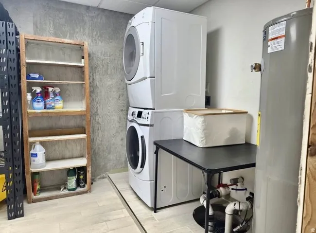 Dedicated utility area featuring a stacked washer and dryer unit, light-toned tile flooring, and a water heater